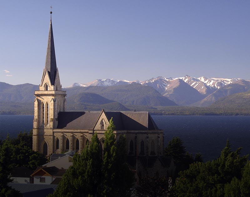 The Nuestra Señora del Nahuel Huapi Cathedral, with a lake and mountains as a backdrop.