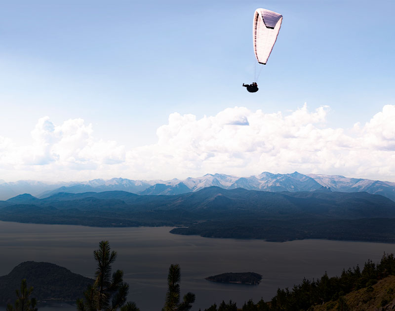 A paraglider soaring over Lake Nahuel Huapi, with beautiful mountain landscapes in the distance.