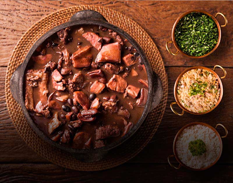 A bowl of feijoada stew, one of Brazil’s most iconic dishes, with some small bowls of toppings.