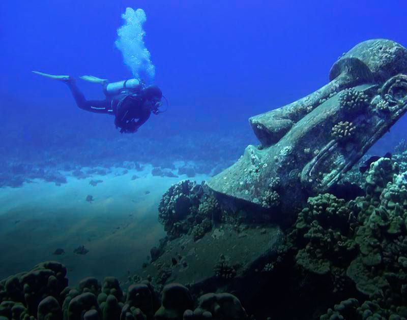 A scuba diver next to a large moai statue located underwater off the coast of Easter Island.