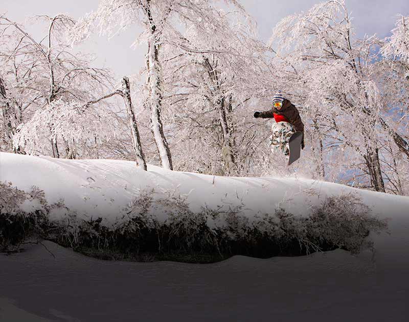 A snowboarder doing a trick in the air on a snowy hill in the Chilean ski resort town of Chillan.