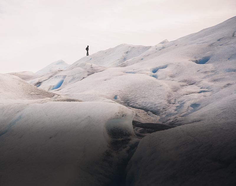 A visitor standing at the summit of an ice-covered hill on top of the Perito Moreno glacier.