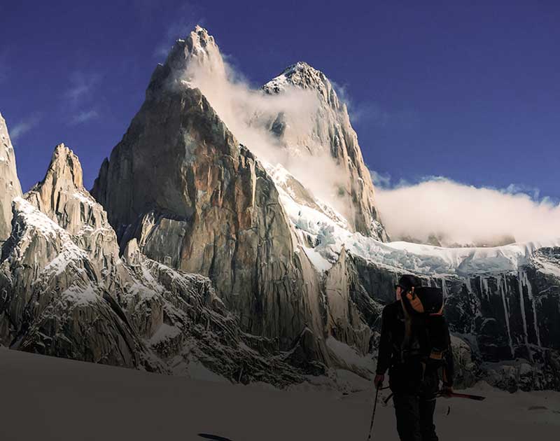 A hiker with a backpack and hiking pole, looking up at the majestic Mount Fitz Roy.