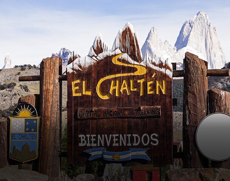 The welcome sign for the town of El Chalten with several mountains visible in the background.
