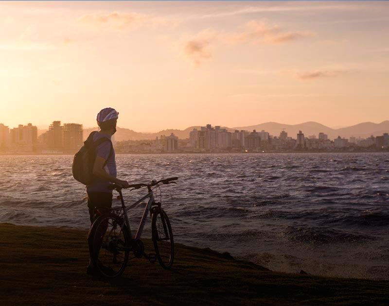 A cyclist standing next to his bike and observing the city from a beach in Florianopolis.