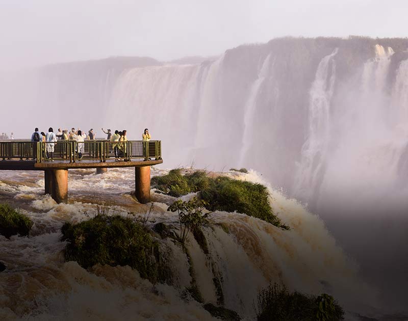 A group of visitors standing on a platform in the middle of a waterfall at the Iguazu Falls.