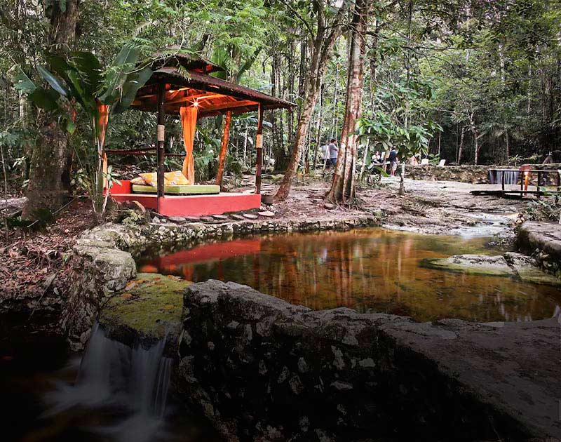 A gazebo with a bed next to a pond and waterfall at the Amazon Ecopark Lodge near Manaus.
