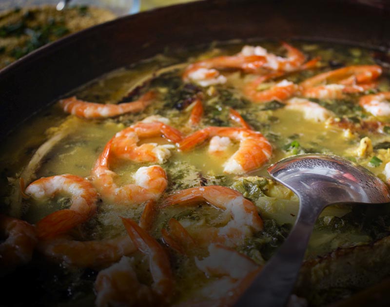 A spoon and a bowl of soup containing shrimp and vegetables at a restaurant in Manaus.