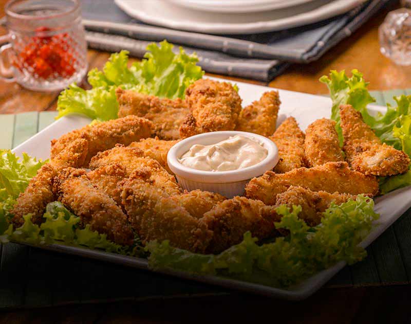 A plate of fried chicken wings on a plate with a cup of dipping sauce at a restaurant in Paraty.