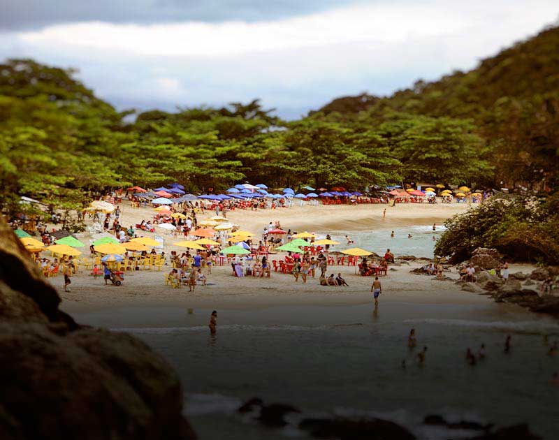 Crowds of people and various-colored umbrellas at Trinidad Beach, surrounded by lush rainforest.
