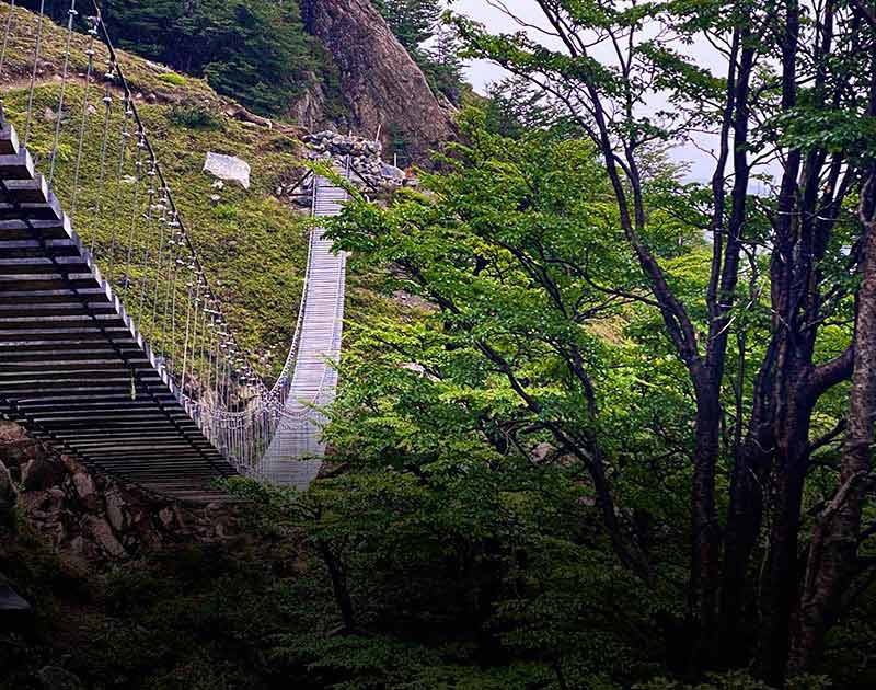 A suspension bridge made of wooden boards crossing a ravine in Torres del Paine National Park.