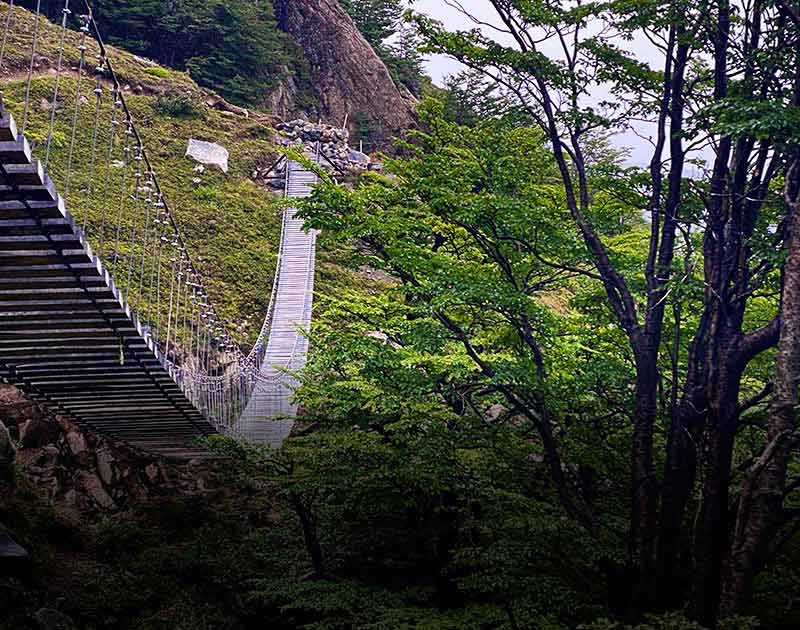 A suspension bridge made of wooden boards crossing a ravine in Torres del Paine National Park.