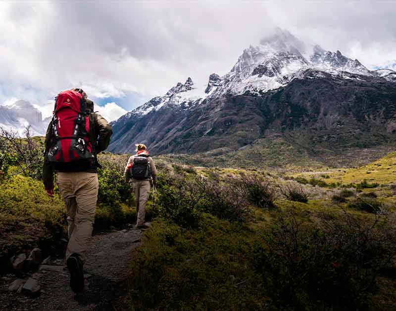 Two hikers with backpacks walking along a trail, surrounded by beautiful mountain landscapes.