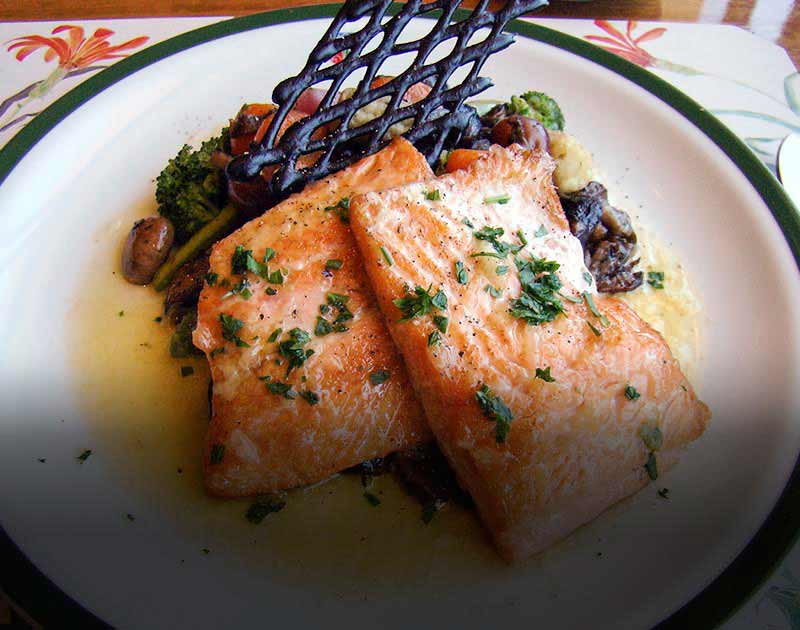 A beautifully-presented plate with two filets of trout served in a sauce with various vegetables.