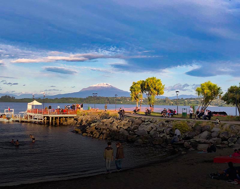 Visitors at a beach and pier in Puerto Varas with the Calbuco Volcano visible in the background.