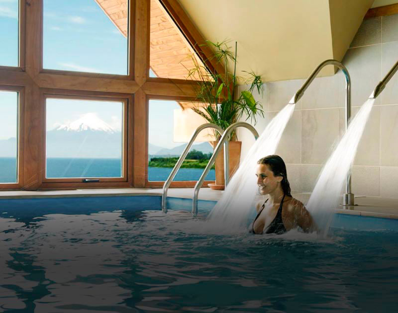 A woman swimming in the pool at Hotel Cumbres, with a view of a lake and volcano out the window.