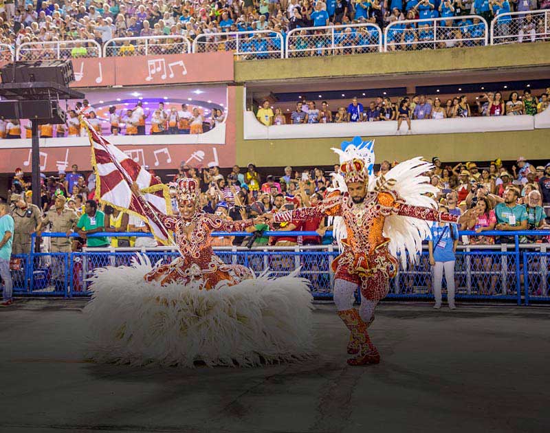 Spectators looking on as dancers dressed in extravagant clothing perform for carnival in Brazil.