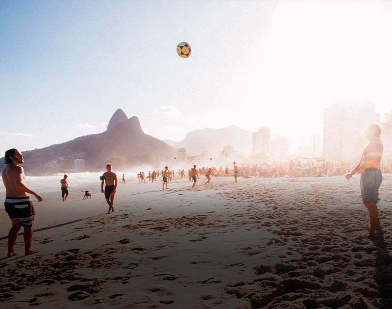 Three men kicking a soccer ball back and forth on Ipanema Beach in Rio de Janeiro.