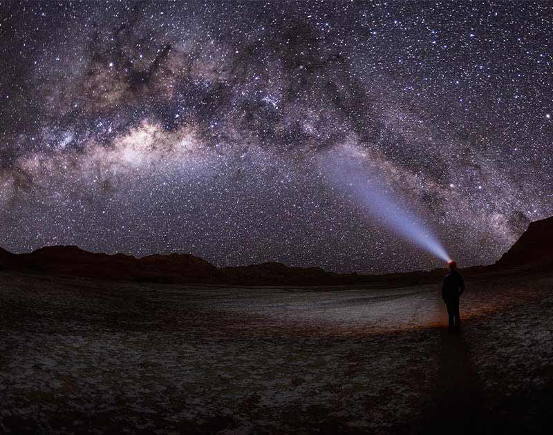 A visitor wearing a headlamp admiring the brilliant night sky over the Atacama desert.