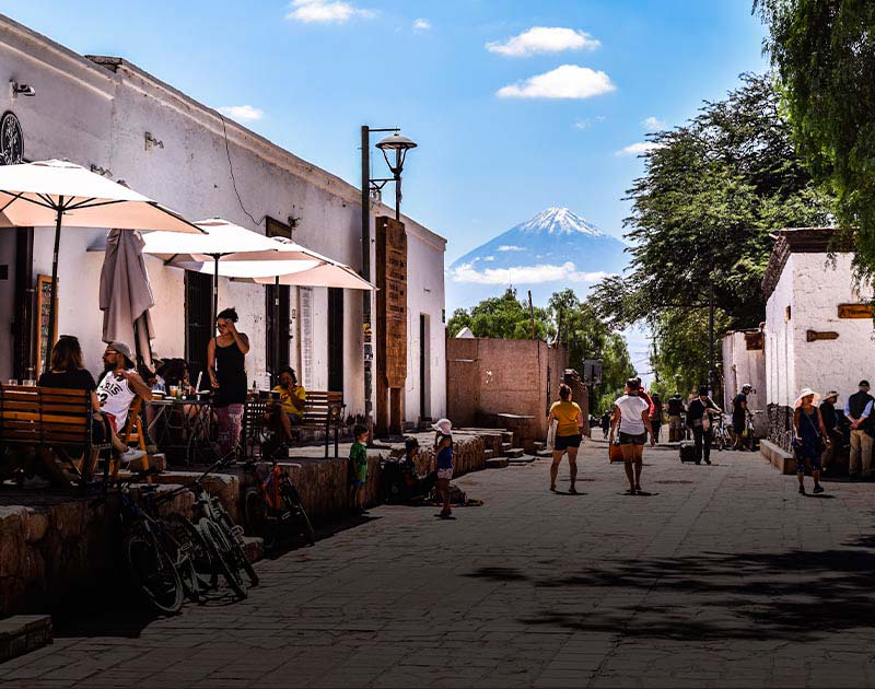 Visitors on a road in San Pedro de Atacama, with a large snow-capped volcano visible overhead.