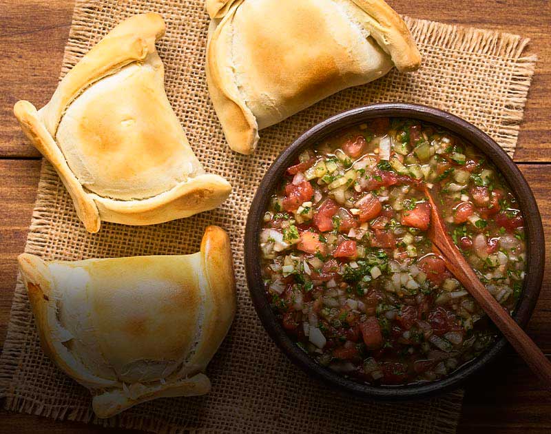 Three empanadas and a bowl of Chilean pebre sauce on a table at a restaurant in Santiago.