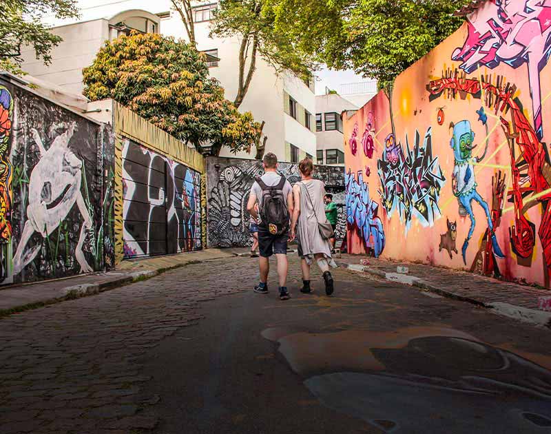 A couple holding hands while walking down an alley filled with street art in Sao Paulo.