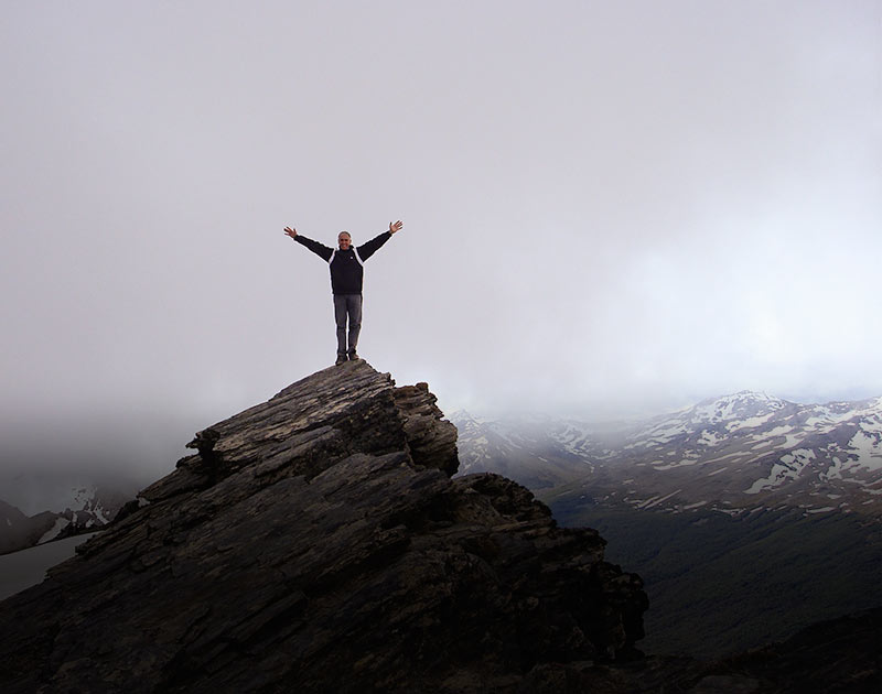 A hiker posing at the summit of Cerro Guanaco, the destination of a popular day hike in Ushuaia.