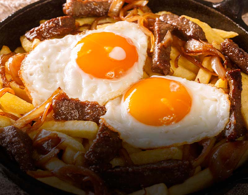 A plate of french fries with beef and onions topped with an egg at a restaurant in Valparaiso.
