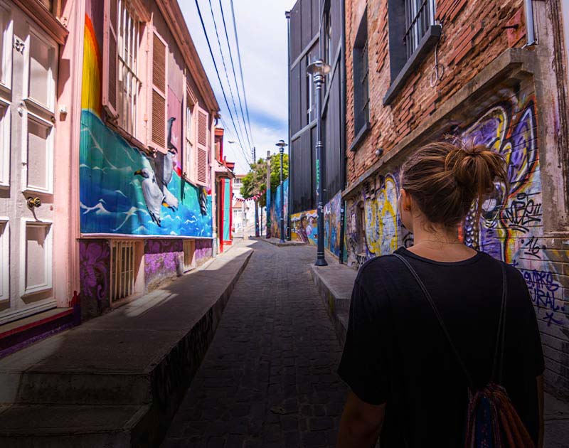A woman with a backpack admiring the colorful street art on the walls of an alley in Valparaiso.