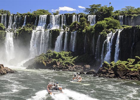 A pair of boats navigating the waters below several waterfalls at the famous Iguazu Falls.