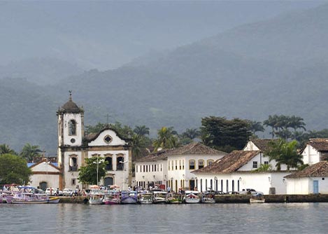 Boats in the water near the St. Rita church in Paraty, with forest-covered hills surrounding.