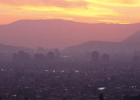 The sun setting over the Santiago skyline, with the Andes Mountains visible in the background.