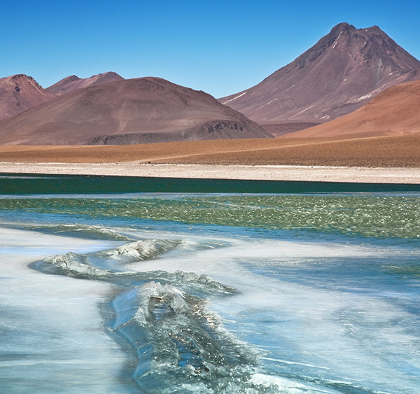 The shimmering water of a lagoon overlooked by red and orange mountains in Chile's Atacama Desert.