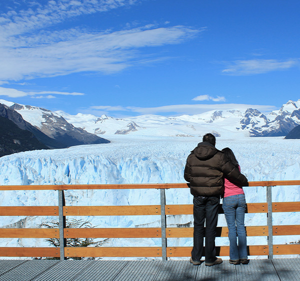 A couple on a walkway looking out at the enormous Perito Moreno glacier in Argentine Patagonia.