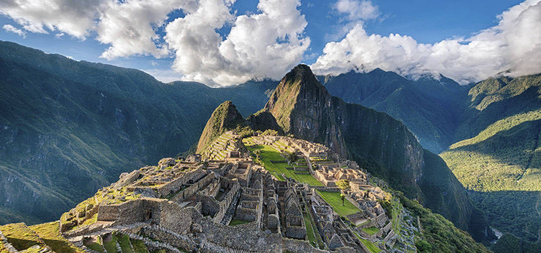 The Inca ruins of Machu Picchu with the Andes Mountains as a backdrop on a partly cloudy day.