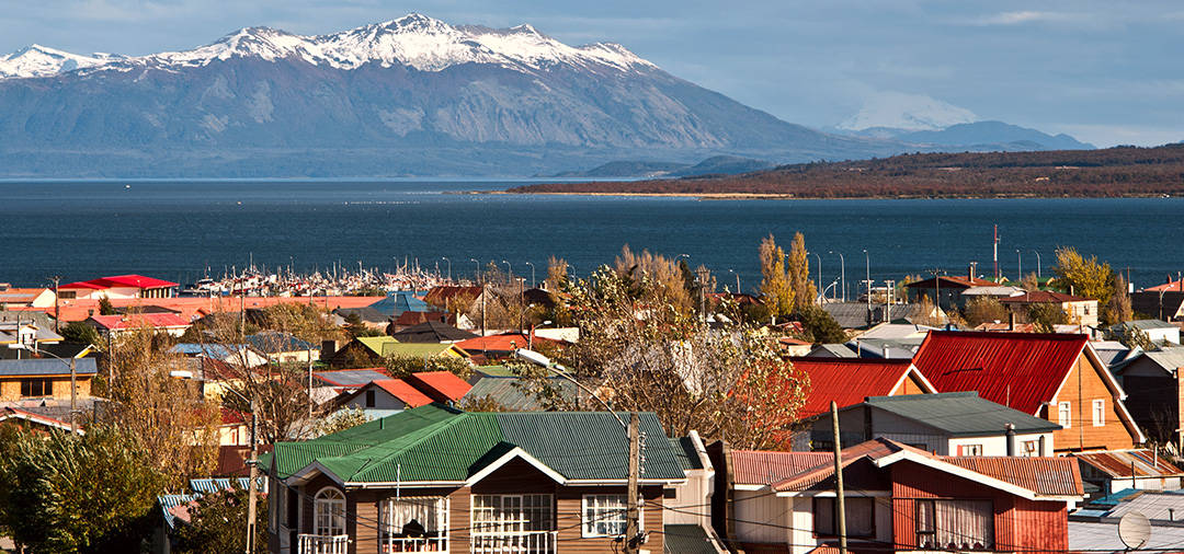 Rooftops of colorful traditional houses with snow-capped mountains overhead in Puerto Natales.