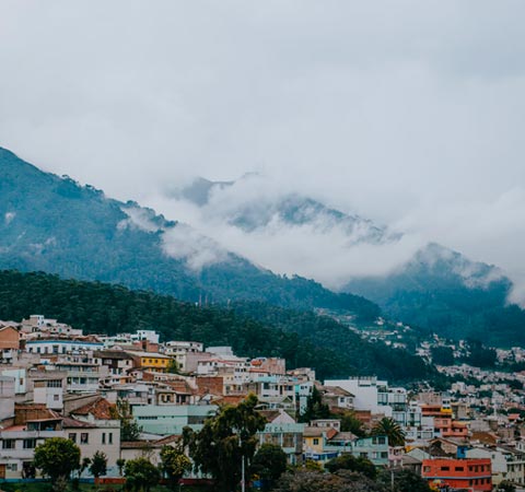 Mountainsides shrouded in clouds and covered in green forest, overlooking the city of Quito.