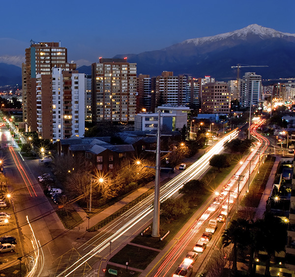 An intersection in Santiago with modern buildings and a snow-capped Andean peak visible.