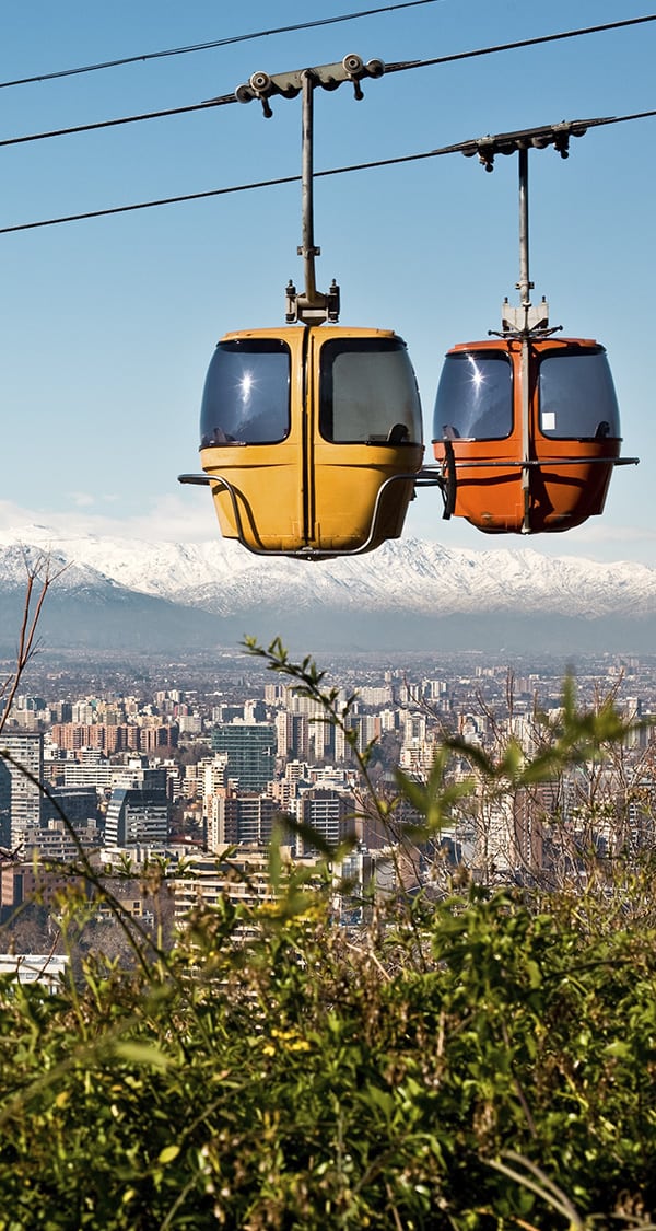 A pair of cable cars overlooking the city of Santiago with the Andes Mountains as a backdrop.