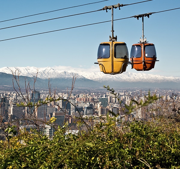 A pair of cable cars overlooking the city of Santiago with the Andes Mountains as a backdrop.