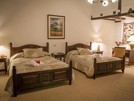 A room with carpeted floor and two beds with wooden frames at the Abraspungo Hotel in Riobamba.