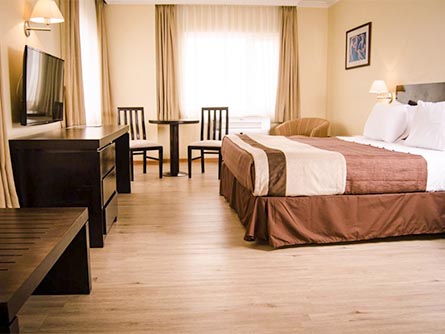 A spacious room with a bed, entertainment center, bench and table at the Hotel Diego de Almagro.