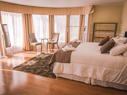 A spacious room with wood flooring and a large bed at the Hotel Lago Sarmiento in Puerto Natales.