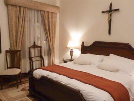 A cozy room at the Hotel San Pedro de Riobamba with classic furnishings and a crucifix on the wall.