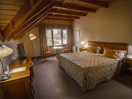 A lovely room with carpeting and a cabin-style wood ceiling at the Kosten Aike in El Calafate.