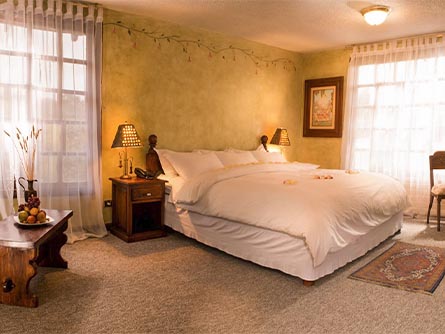 A room with carpeted floor, a large bed, and wooden furniture at the La Andaluza Hotel in Riobamba.