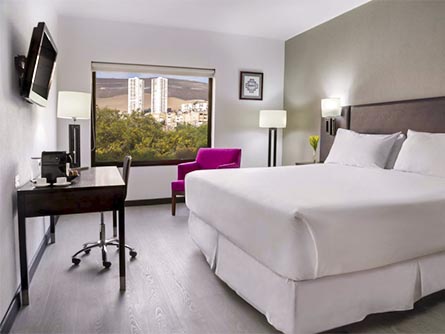 A room at the NH Iquique hotel with mostly white and black decor except for a bright pink chair.