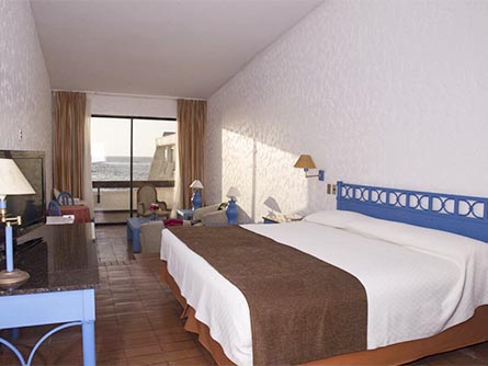 A spacious room with wood floors and a large bed at the Panamericana Hotel in Arica.