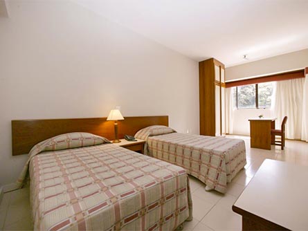 A spacious room with wooden furniture and two double beds at Porto Farol Apart Hotel in Salvador.