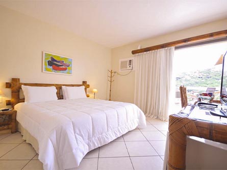 A room with tile floors, a large bed, and wood furnishings at the Rio Buzios Beach Hotel.